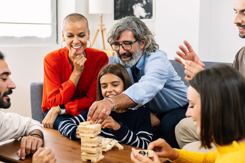 A group of people gathered around a table playing a game with wooden blocks, embracing a digital detox. They appear engaged and smiling, enjoying the benefits of reduced screen time for their wellbeing.