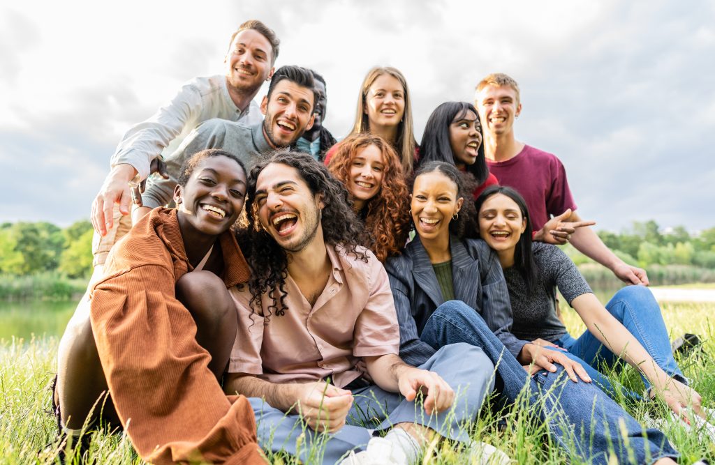 A group of ten people sitting and smiling on a grassy field by the lake, with trees and a cloudy sky framing this perfect Sample Post #3.