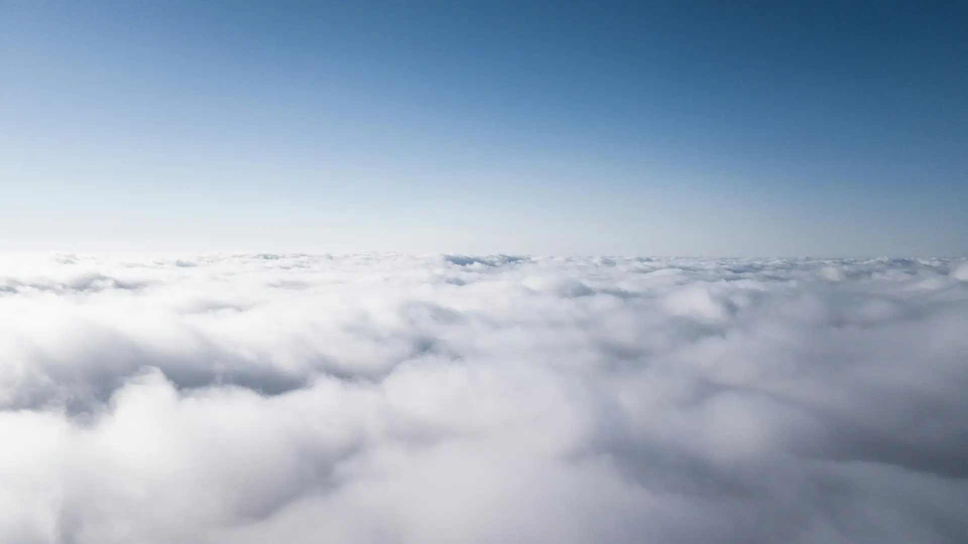 Fluffy white clouds spread across a wide expanse under a clear blue sky.
