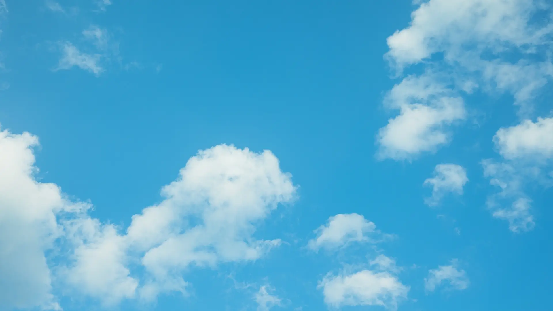 A clear blue sky with scattered fluffy white clouds.