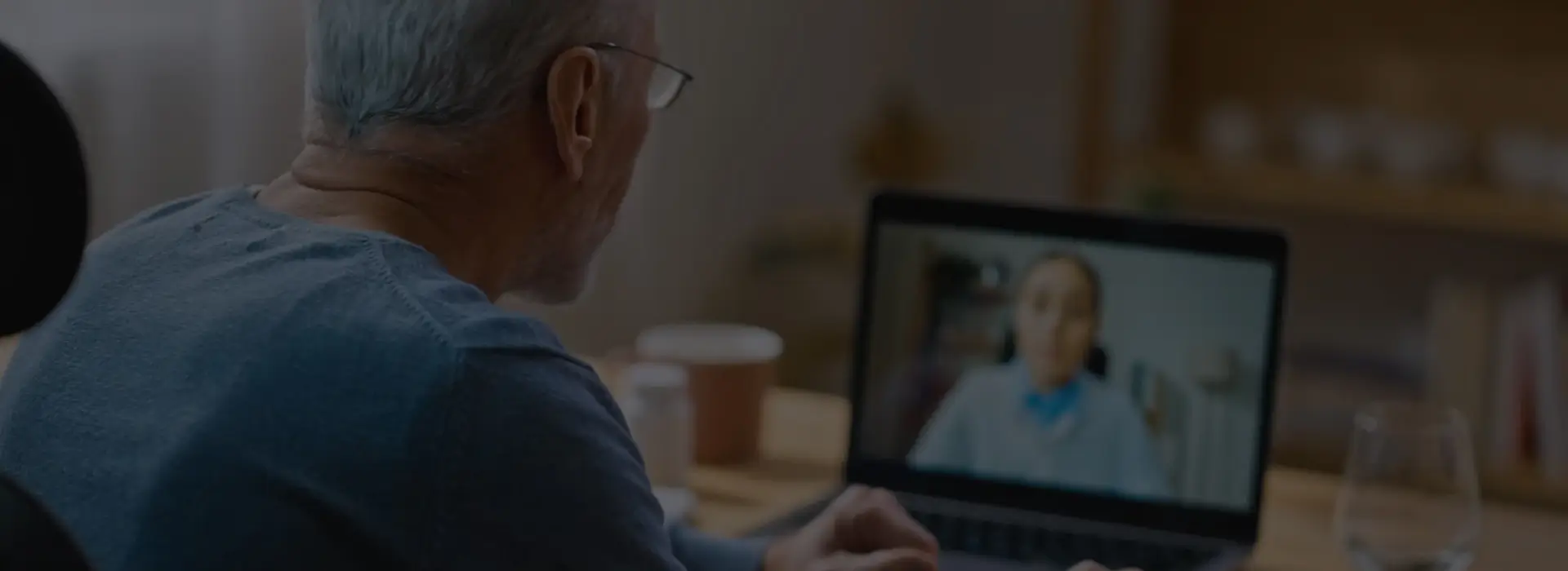Elderly man with glasses having a video call on a laptop.