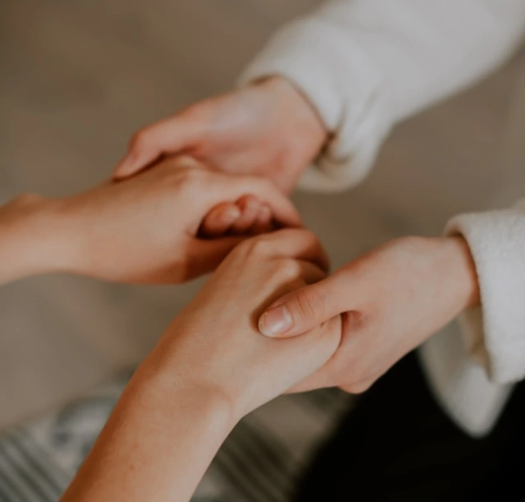 Two people holding hands gently, with one person's hands wrapped around the other's.